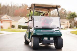 Hombre mayor activo conduciendo un carrito de golf en una carretera vecinal. -Leyes para Conducir Carros de Golf en Los 50 Estados